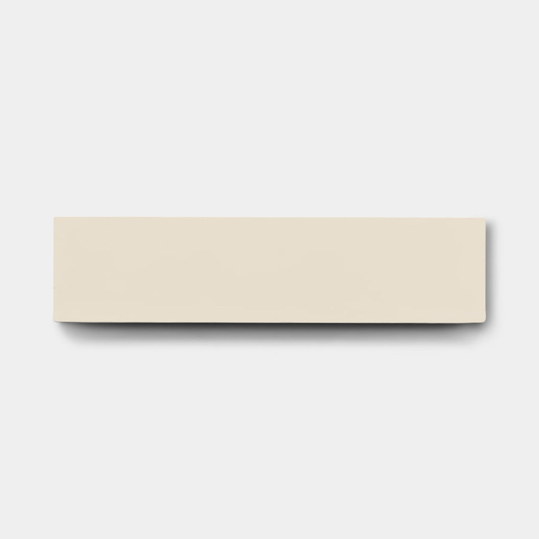 A rectangular, off-white Bone 2x8 tile sample by vendor-unknown lies centered on a plain light gray background, casting a faint shadow below and to the right—echoing the clean lines of handmade tiles.