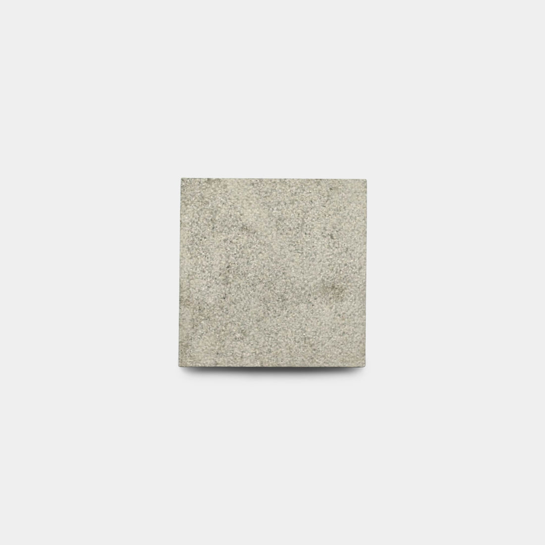 The Monument 6x6 + Bush Hammered sample by Zia Tile is a square, light gray handmade stone tile with a slightly rough texture, showcasing subtle elegance inspired by classic Moroccan design.