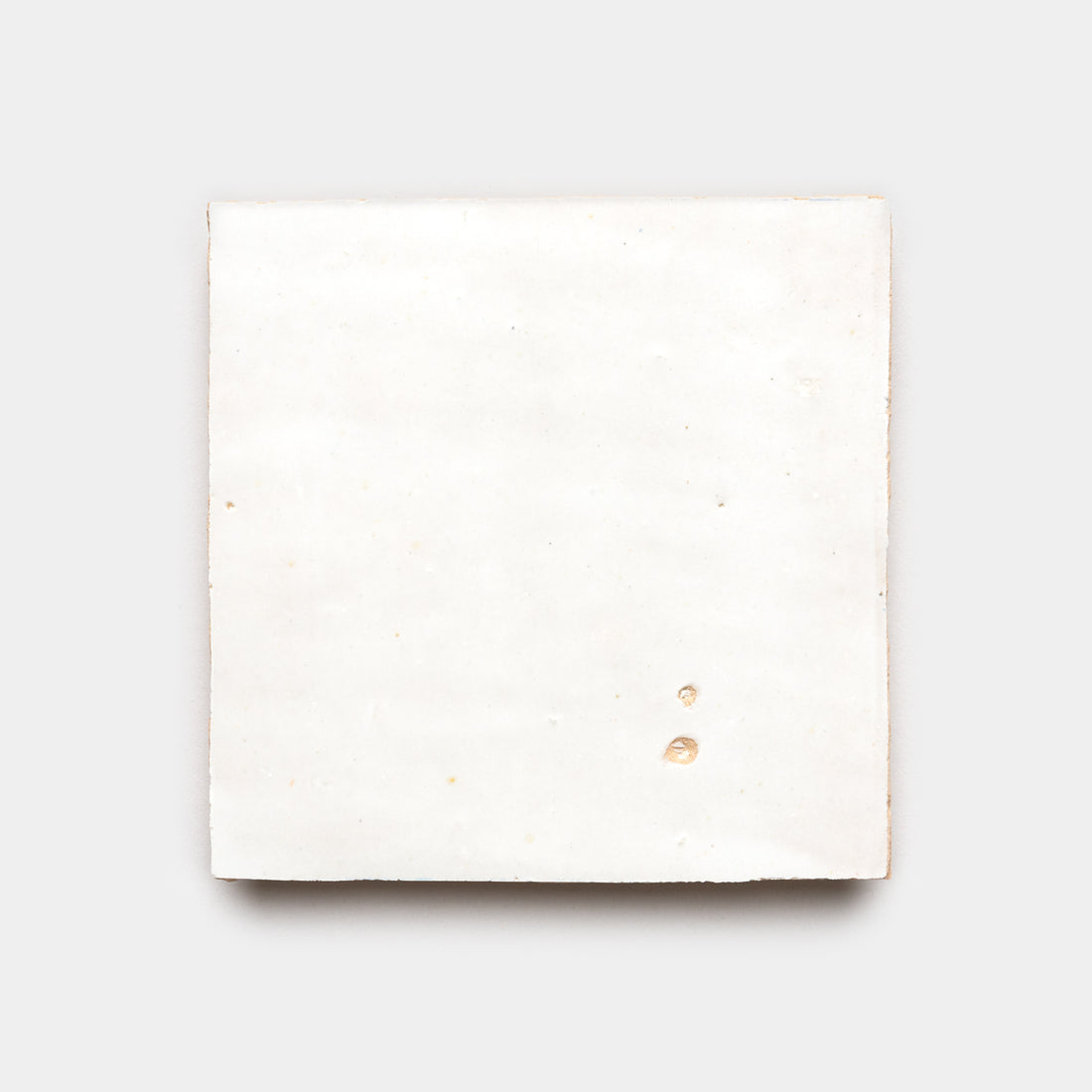 A single Pure White 4x4 ceramic tile by Zia Tile, in off-white with a smooth surface and slight imperfections, such as two small dents at the bottom right, displayed on a plain light gray background.