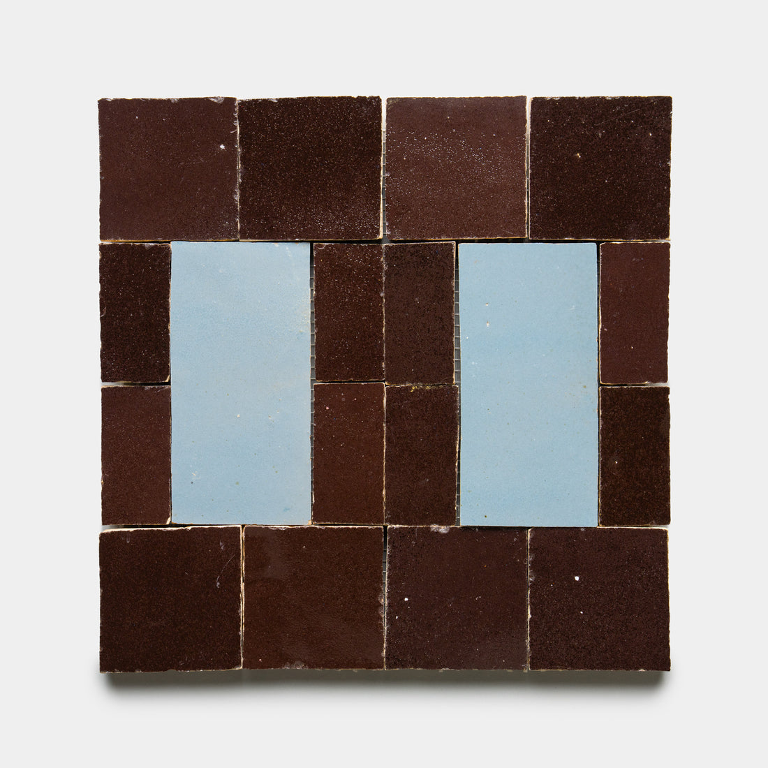 The Souk 2 tile by Zia Tile features a geometric, symmetrical pattern with a dark brown border and two vertical light blue rectangles centered on a white background.