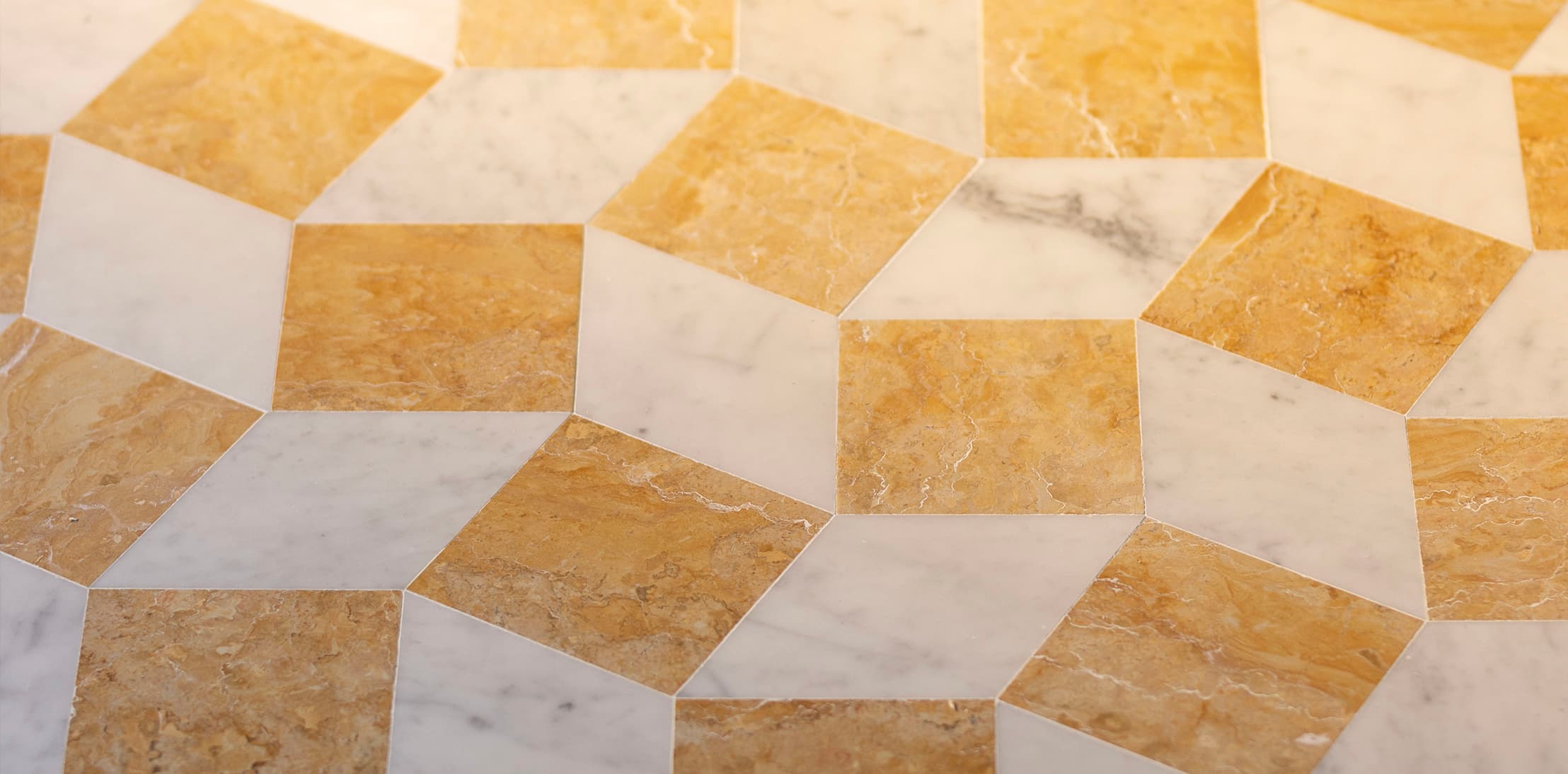 A geometric pattern of interlocking cubes made from yellowish-brown and white marble tiles, creating a 3D optical illusion on a flat surface.