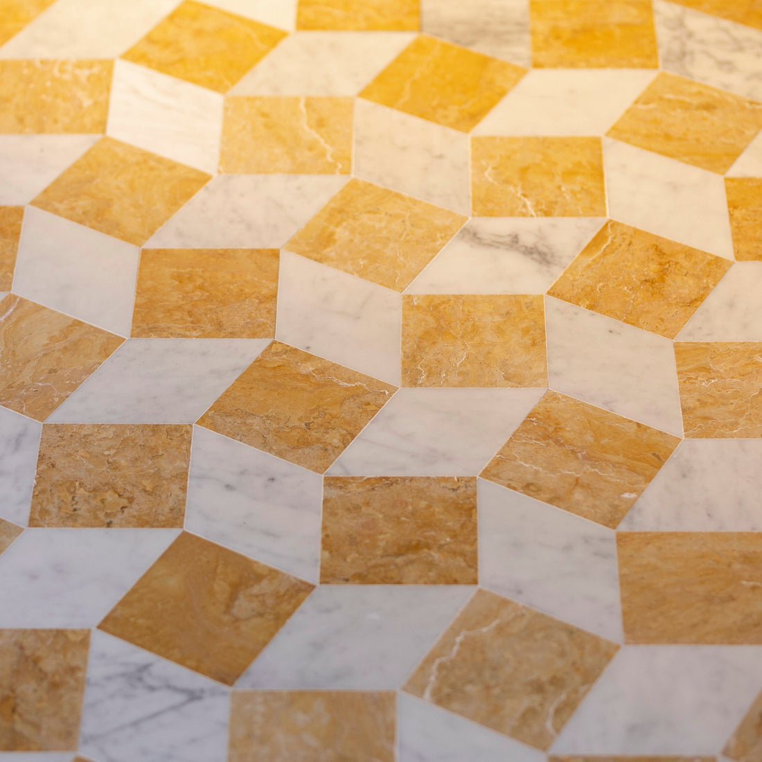 Lombardy in Carrara + Giallo Reale by Zia Tile features a geometric pattern with alternating yellow-brown and white ceramic tiles, arranged in a three-dimensional cube illusion for a bold, tessellated effect.