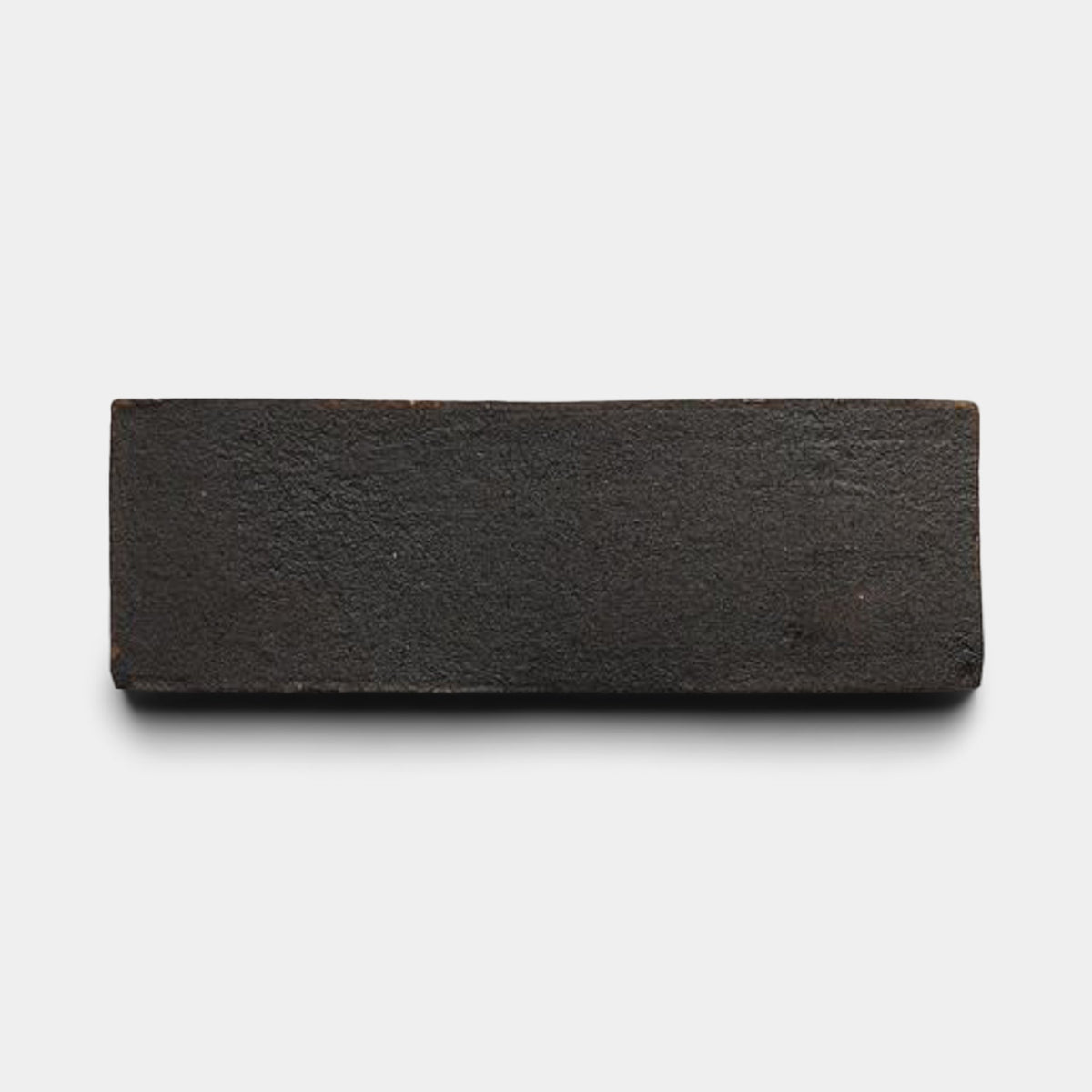 A single 2x6 Rectangle + Oscura sample by Zia Tile, featuring a dark brown, rough handmade texture, is displayed against a plain white background.