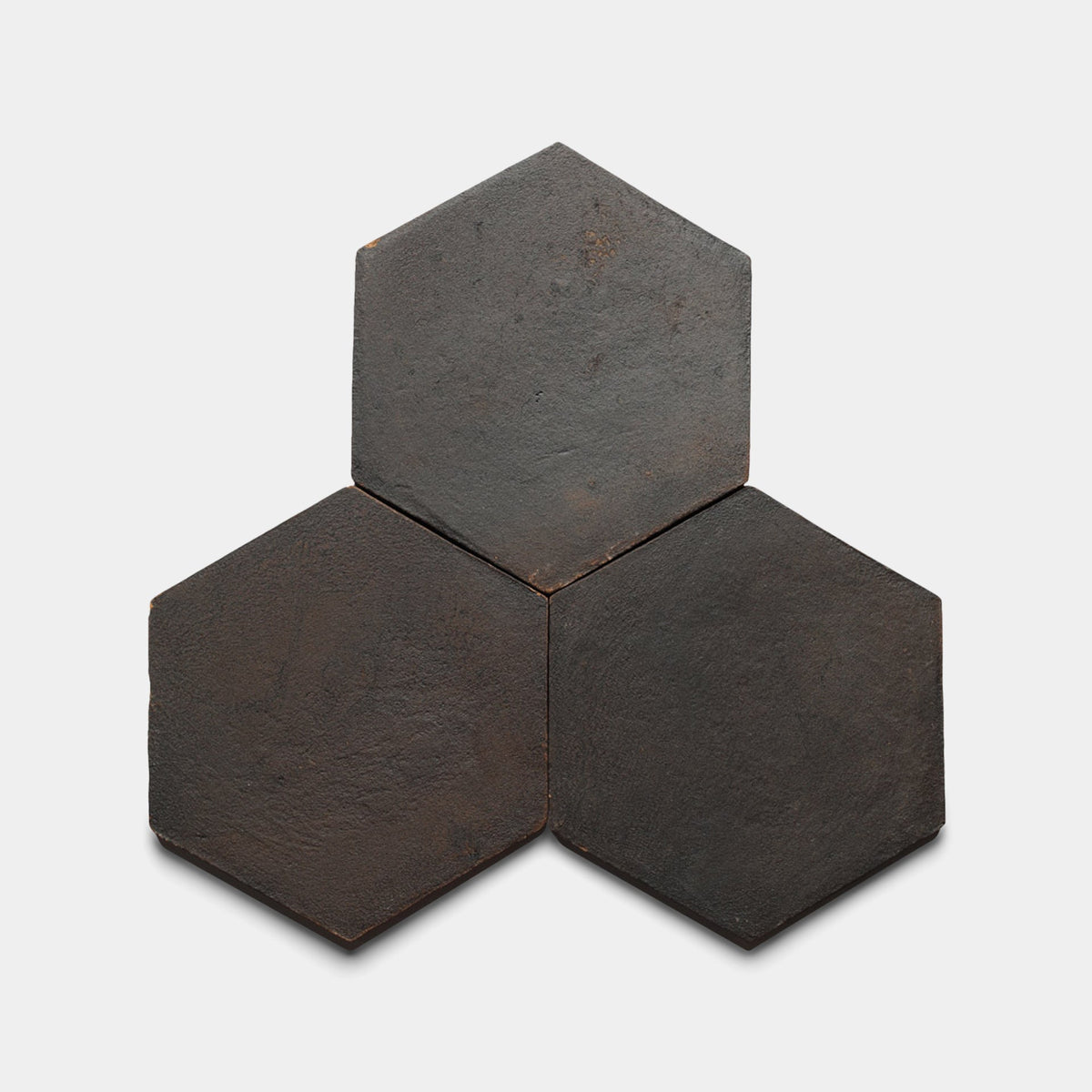 Three 8x9 Hex + Oscura sample tiles by Zia Tile, dark and hexagonal with a slightly rough matte finish, are arranged in a triangular pattern on a light gray background.