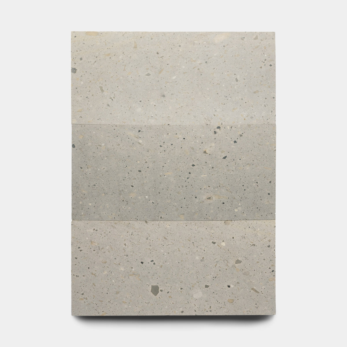 Acacia 12x24 by Zia Tile is a rectangular light gray terrazzo tile inspired by Mexican Cantera, featuring three horizontal sections with small gray and beige specks on a white background.