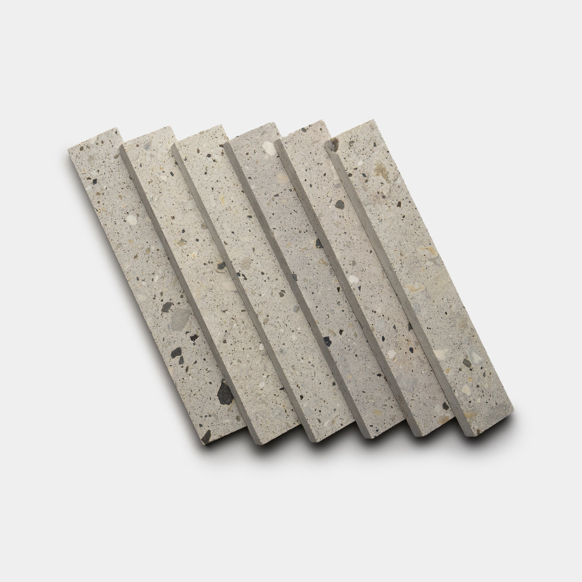 Six Acacia 2x12 terrazzo tiles by Zia Tile, featuring a speckled gray surface, are arranged diagonally in a neat, slightly staggered stack on a plain white background.