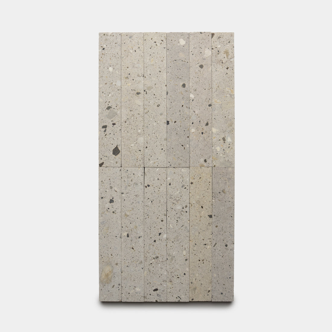Sixteen vertically stacked Acacia 2x12 terrazzo tiles by Zia Tile, featuring light gray color with scattered darker speckles, arranged in a rectangular layout against a plain white background.