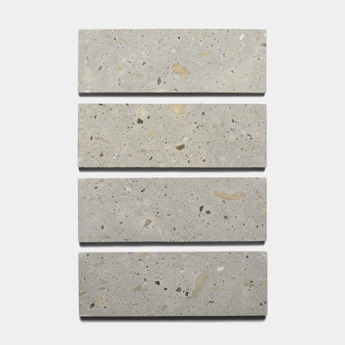 Four Acacia 4x12 rectangular tiles by Zia Tile, featuring a speckled terrazzo-like surface, are arranged vertically against a white background.