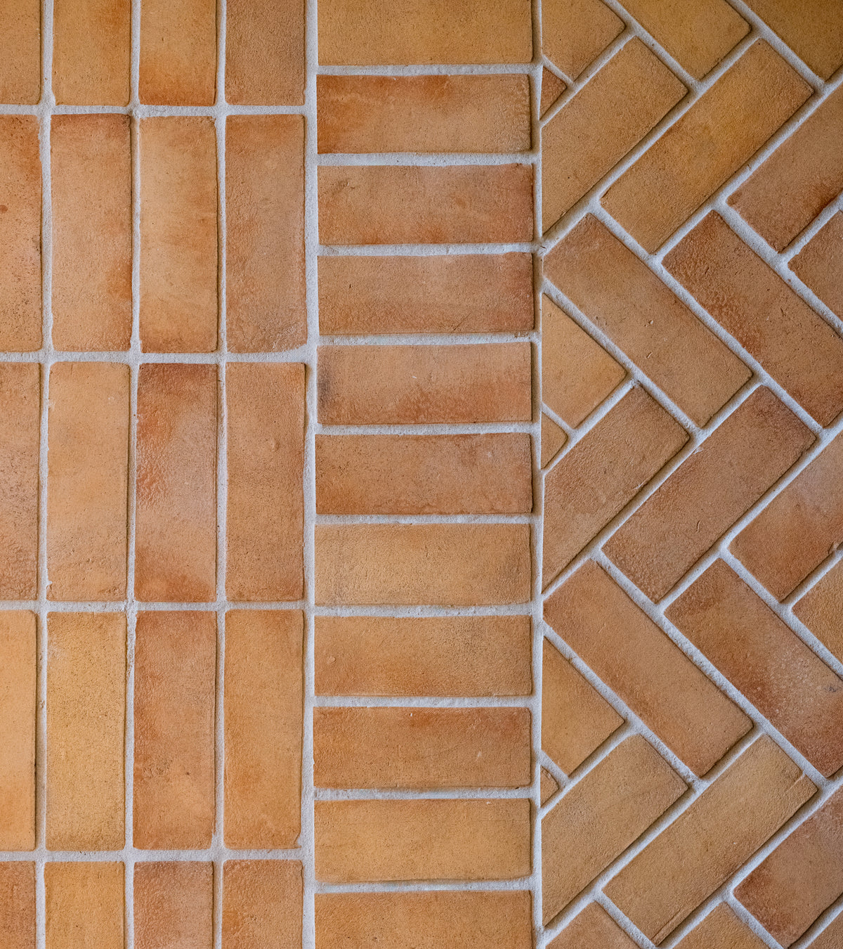 Close-up of Zia Tile’s 2x6 Rectangle + Adobe, tan and brown handmade ceramic tiles inspired by San Miguel de Allende, shown in a straight layout on the left and herringbone on the right, divided by diagonal grout lines.