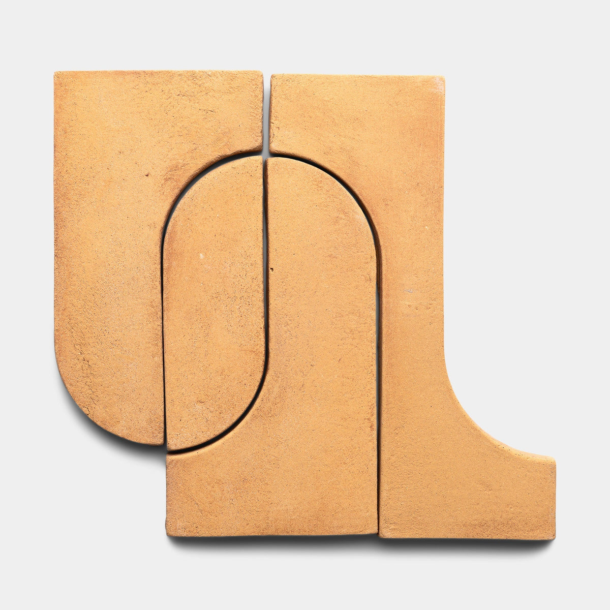Four tan Durango + Adobe tiles from Zia Tile fit together in an abstract geometric pattern of curved and straight edges, resembling interlocking shapes on a light gray background.