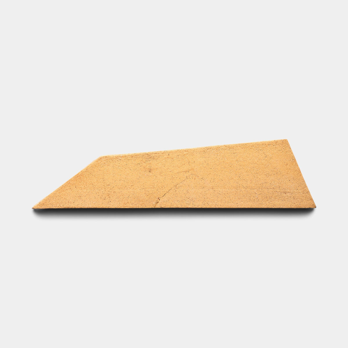 A single Tornillo + Adobe, Sample ceramic tile by Zia Tile is displayed on a plain white background, casting a soft shadow beneath its light brown trapezoid shape.
