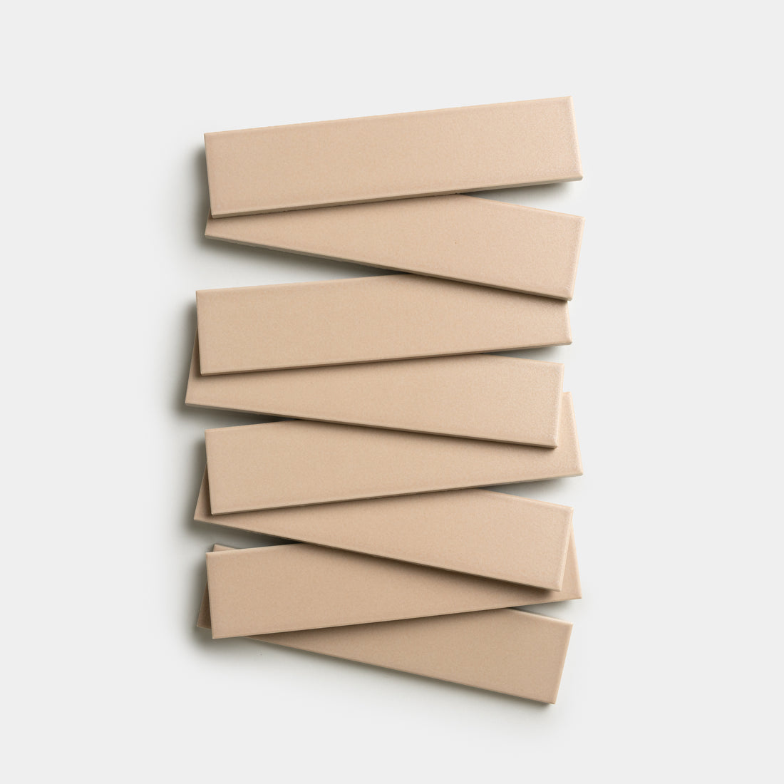 Seven Afterglow 2x8 rectangular tiles from Zia Tile, in a beige color, are arranged in a staggered zigzag pattern on a plain white background.