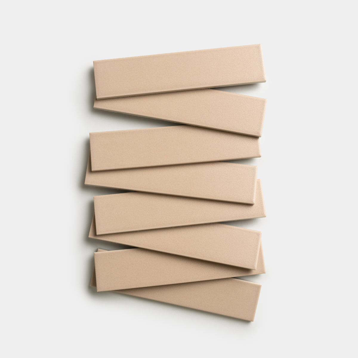 Seven Afterglow 2x8 rectangular tiles from Zia Tile, in a beige color, are arranged in a staggered zigzag pattern on a plain white background.