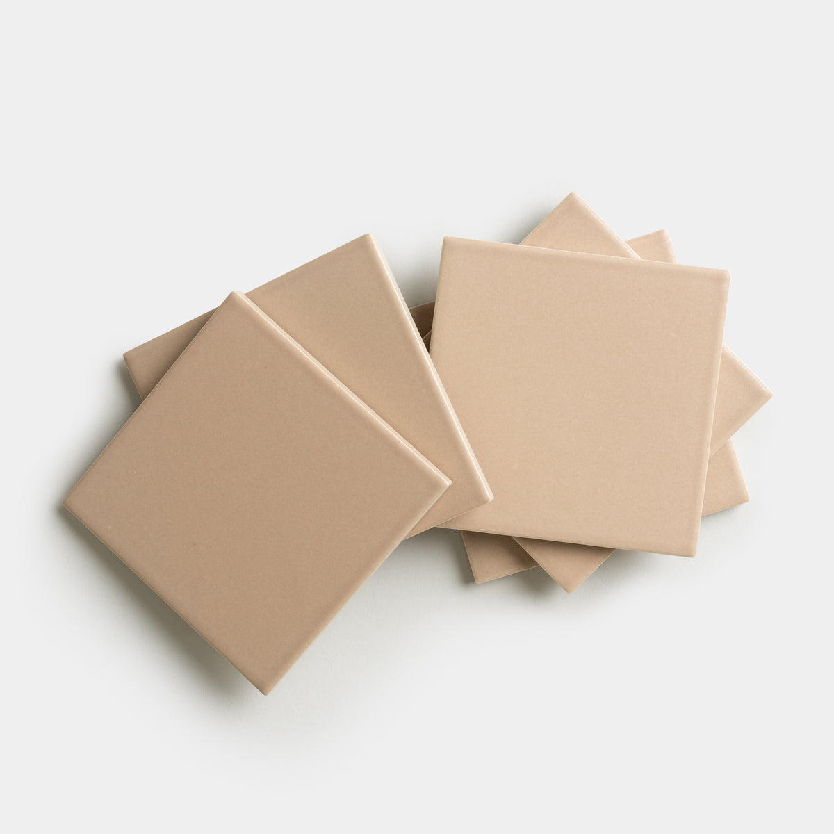 Six Afterglow 4x4 ceramic tiles by Zia Tile in light beige are arranged in a slightly overlapping, fanned-out pattern on a white background.