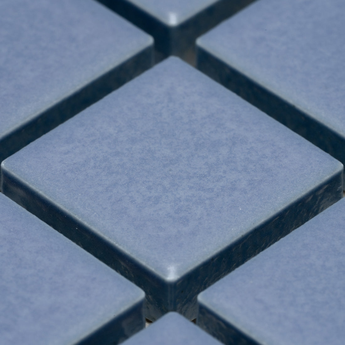 Close-up of Zia Tile’s Aizome 1x1 blue square ceramic tiles, arranged in a grid with visible grout lines and a slightly textured surface.