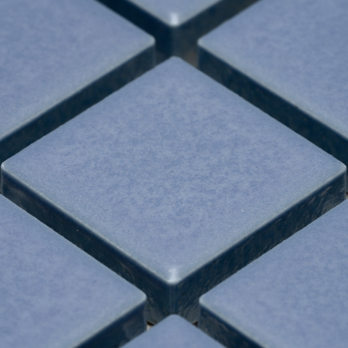 Close-up of Zia Tile’s Aizome 1x1 blue square ceramic tiles, arranged in a grid with visible grout lines and a slightly textured surface.