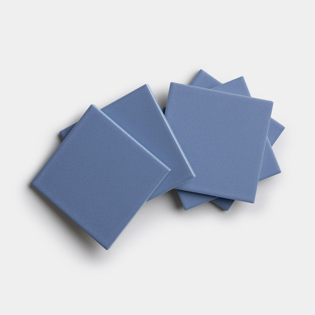 Five glossy, square Aizome 4x4 blue ceramic tiles by Zia Tile are stacked and slightly fanned out on a white background.