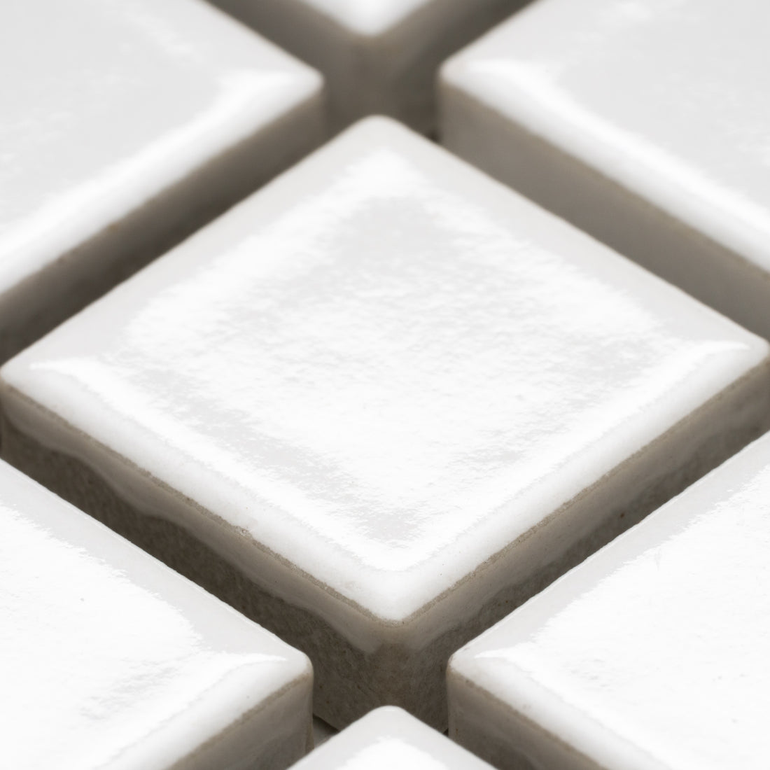 Close-up of Zia Tile's Alabaster White 1x1 ceramic tiles, arranged in a diamond pattern with visible grout lines. The glossy white surface is smooth and slightly reflective.