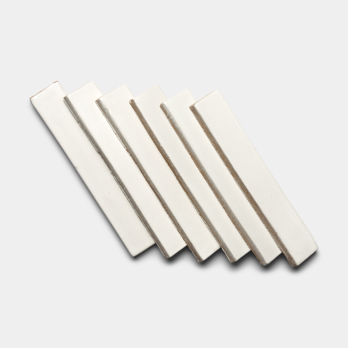 Five Albar Mini Bar tiles by Zia Tile, in a rectangular off-white ceramic design, are displayed diagonally and overlapping on a light gray background.
