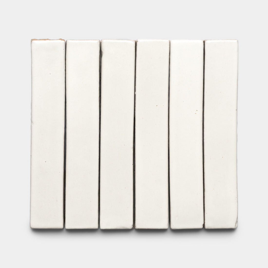 Seven Albar Mini Bar white ceramic tiles by Zia Tile are arranged vertically side by side on a light gray background, creating a tidy, grid-like display.