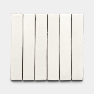 Seven Albar Mini Bar white ceramic tiles by Zia Tile are arranged vertically side by side on a light gray background, creating a tidy, grid-like display.