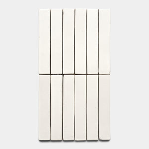 Fourteen Albar Mini Bar tiles by Zia Tile are arranged in two neat rows of seven on a light gray background, forming a closely aligned, grid-like pattern with their rectangular white shapes.