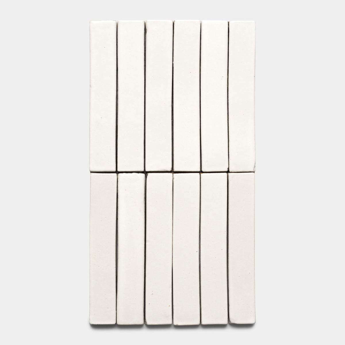 Fourteen Albar Mini Bar tiles by Zia Tile are arranged in two neat rows of seven on a light gray background, forming a closely aligned, grid-like pattern with their rectangular white shapes.