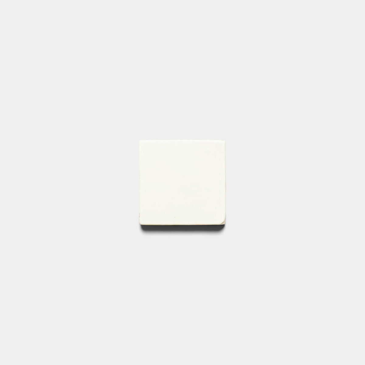 A small Albar 4x4 Square sample by Zia Tile, in plain white, sits centered on a light gray background with a faint shadow beneath it.