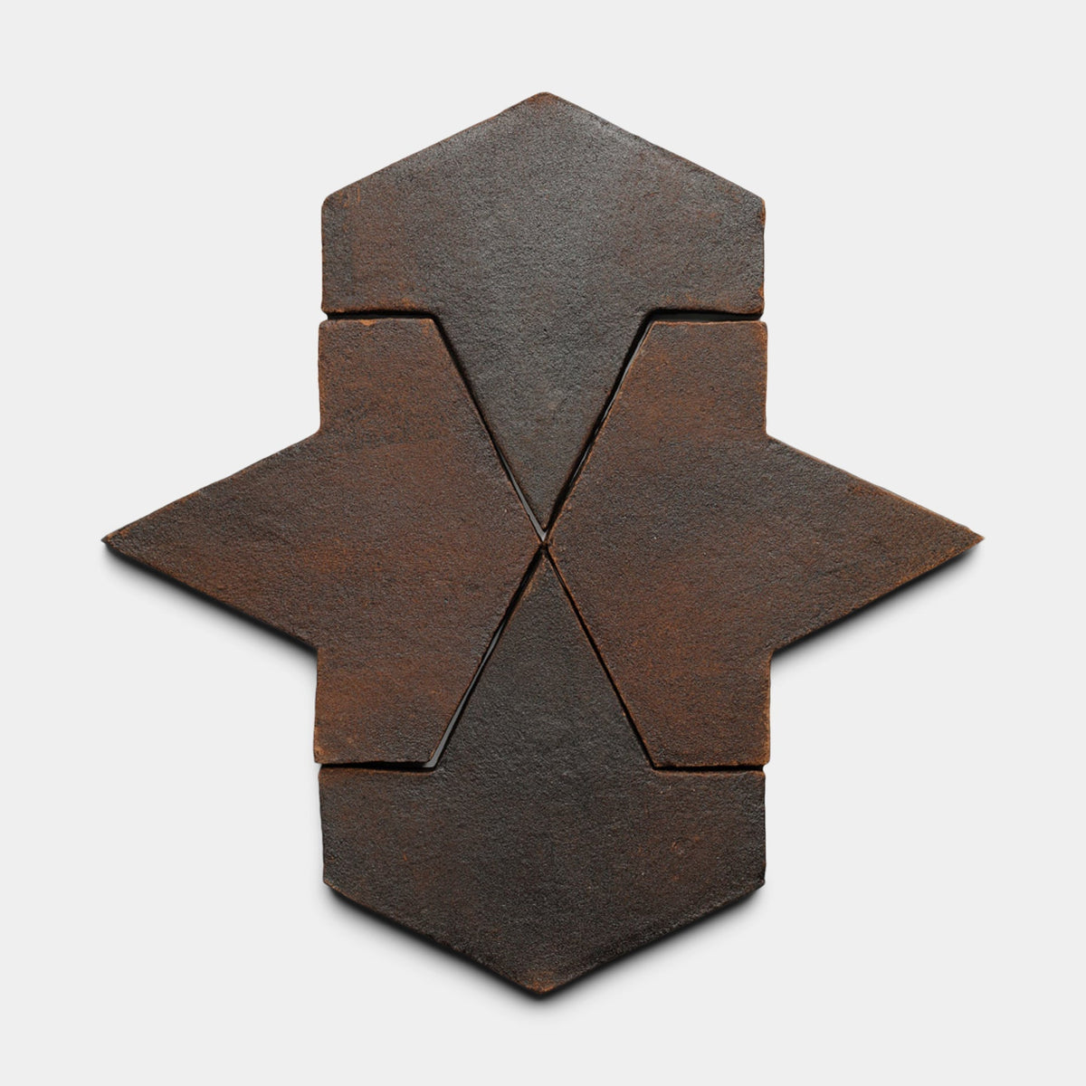 A set of five dark, rust-colored Alcazar + Madera tiles by Zia Tile forms a symmetrical, star-like geometric pattern on a light background.