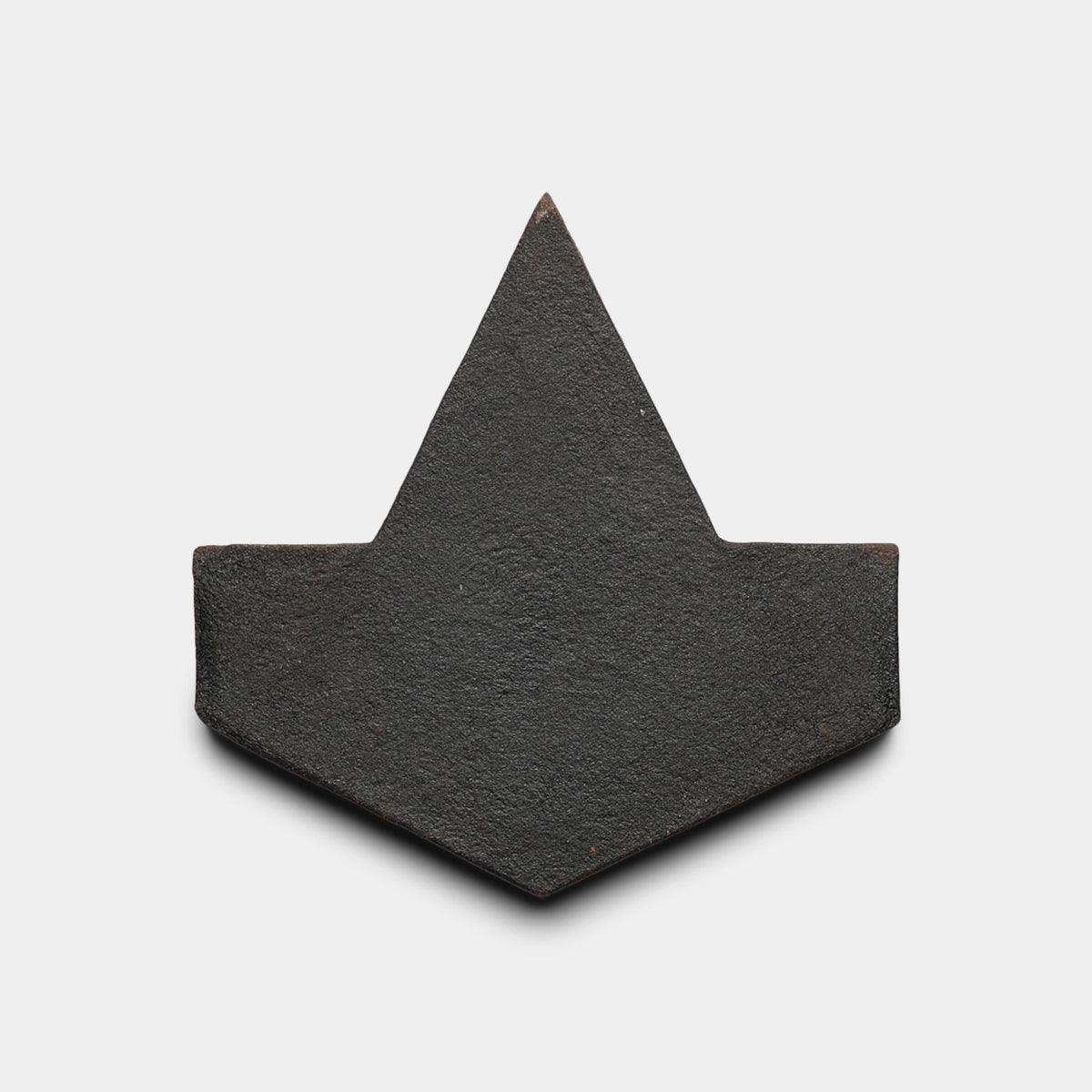 A flat, black geometric tile sample—Alcazar + Oscura by Zia Tile—features an arrowhead or house-like shape with a pointed top and wide base, set against a plain white background.