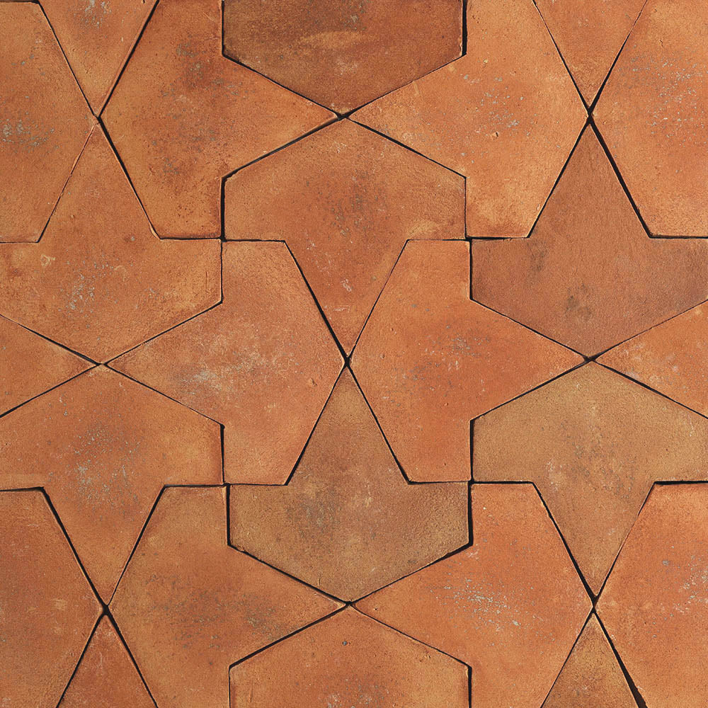 A close-up of Big Alcazar + Fired Earth tiles by Zia Tile showcases reddish-brown terracotta interlocking tiles in a star-like geometric pattern, featuring a natural, slightly textured finish.