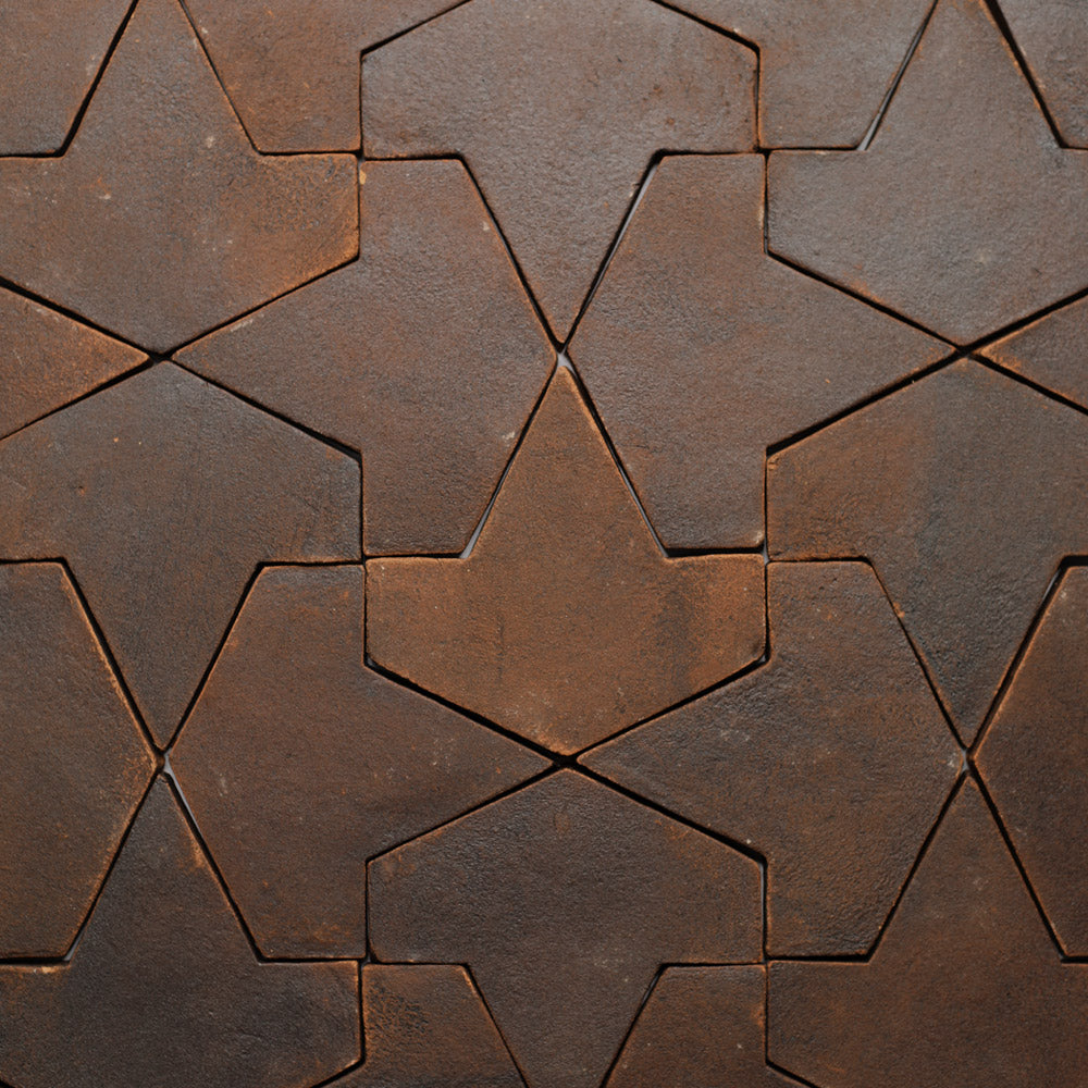 Close-up of Zia Tile’s Alcazar + Madera sample, showcasing handmade Moroccan tiles with interlocking star and arrowhead patterns. The matte finish and varying brown tones add texture and depth to the geometric surface.