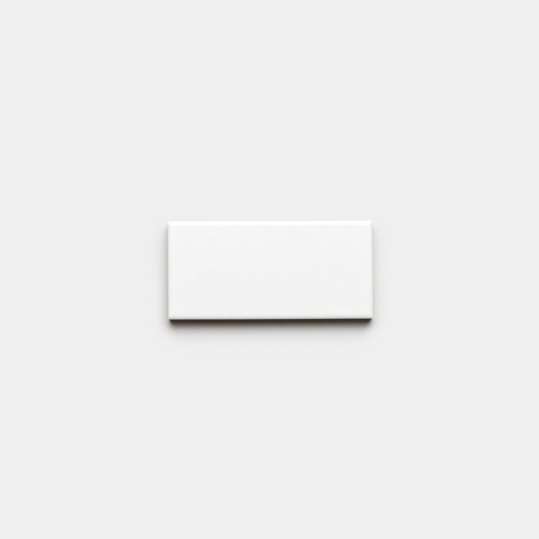 A single Alpha White 2x4 matte ceramic tile by Zia Tile is centered on a plain light gray background.