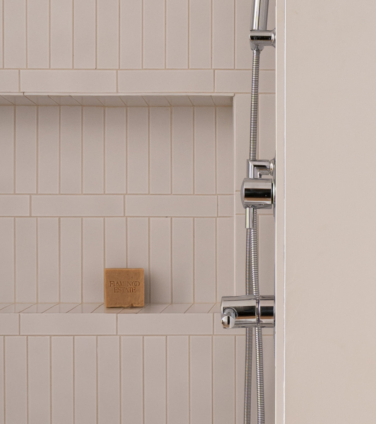 A modern shower featuring Alpha White 2x8 matte architectural grade ceramic tile by Zia Tile, a built-in shelf with a brown soap bar, and a partially visible silver shower fixture on the right.
