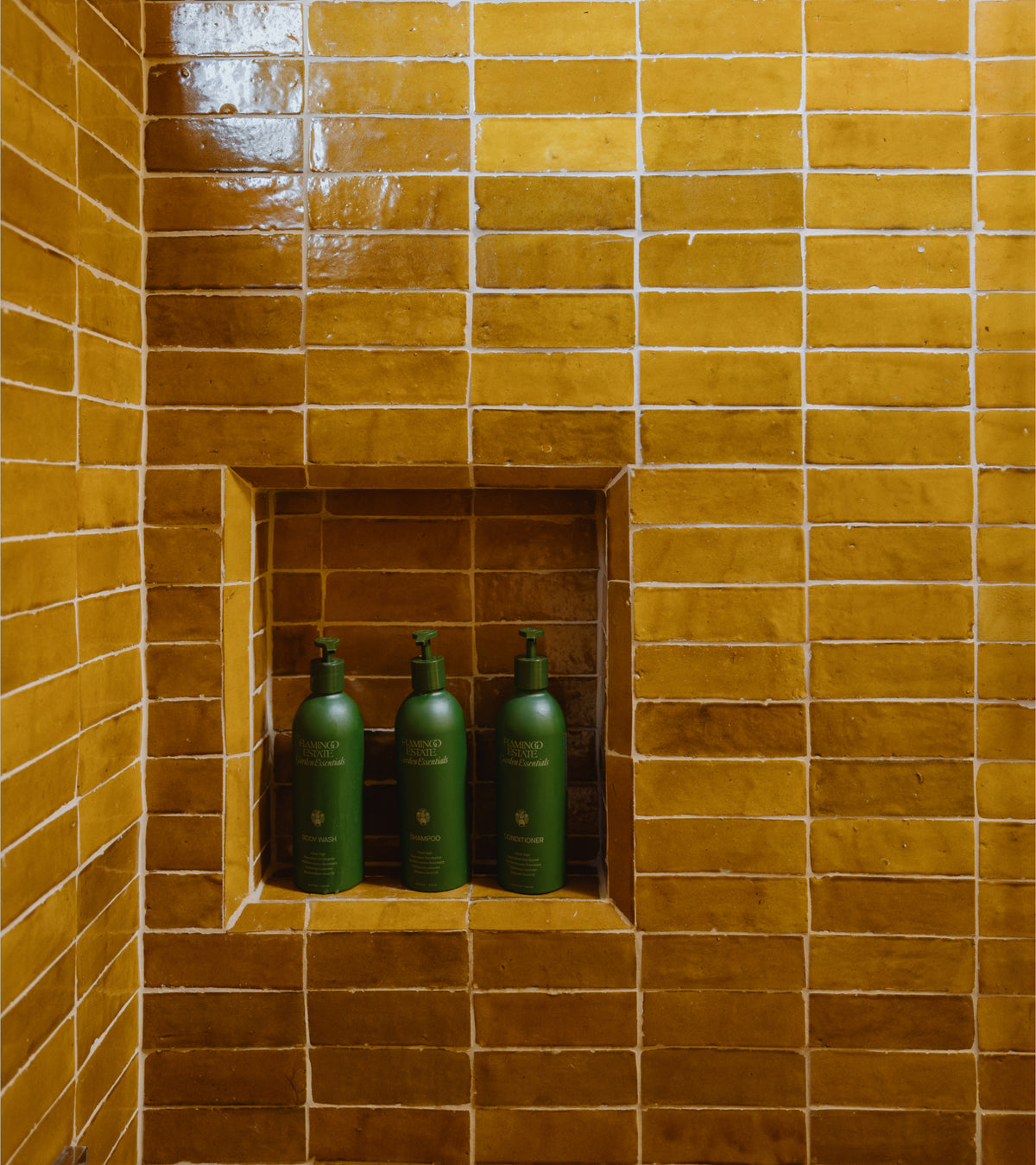 Zia Tile Amber 2x6 zellige tiles are installed on a shower wall with a built-in recessed niche holding three green bottles.