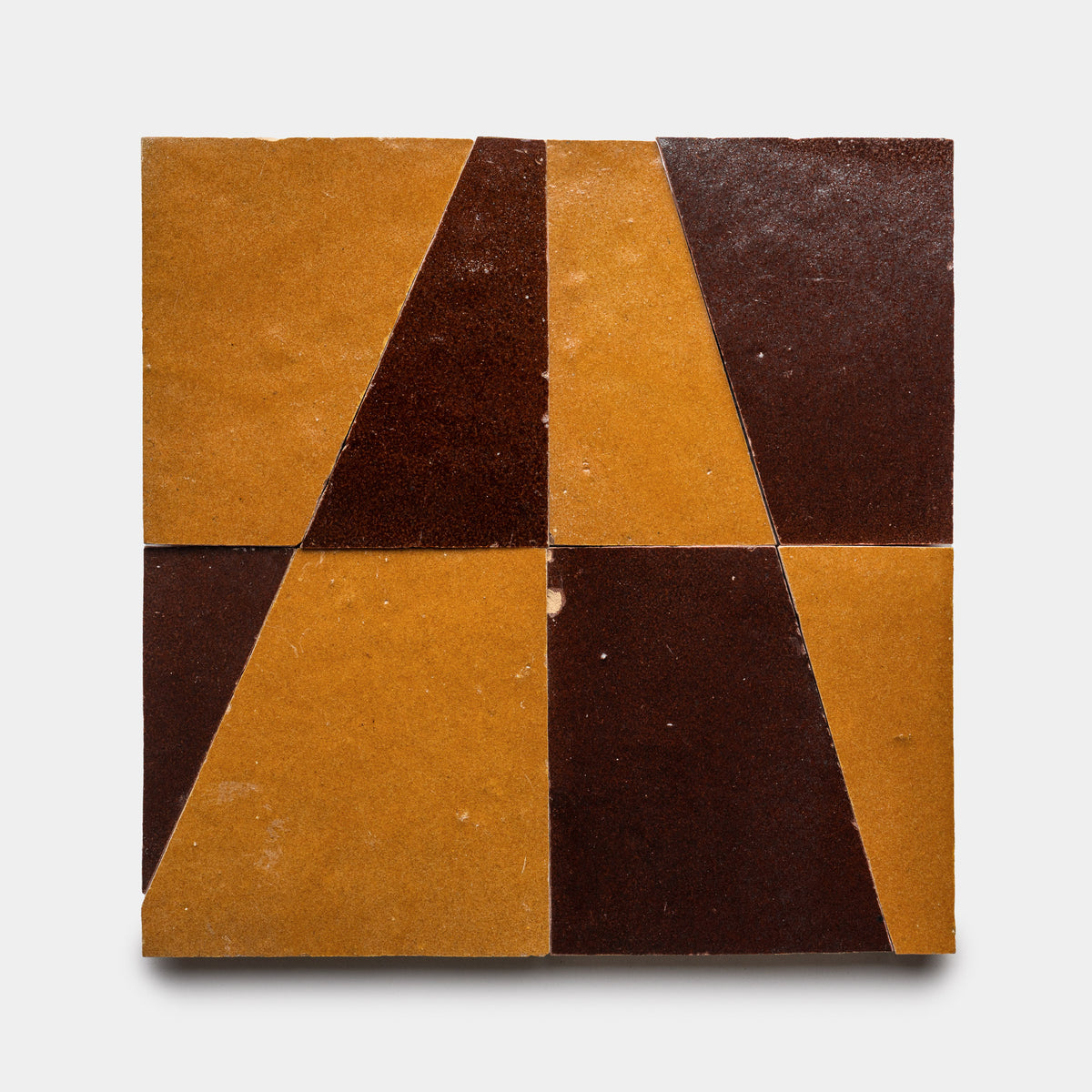 Atlas 2 by Zia Tile features a square tile made of four smaller tiles, each split diagonally into brown and golden-yellow triangles for a bold geometric look. The surface is subtly textured, adding depth to its abstract pattern.