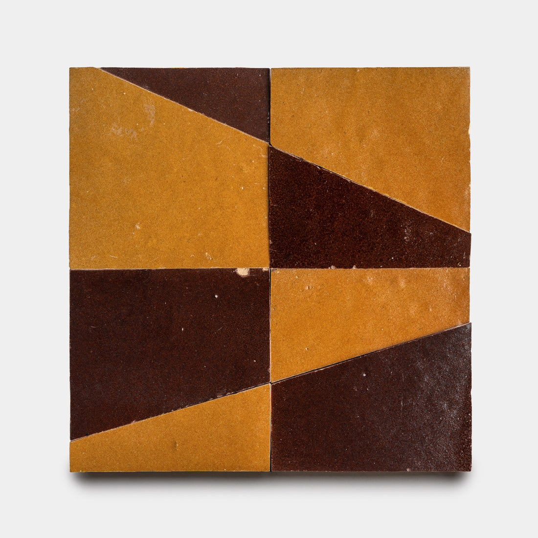 The Atlas 2 by Zia Tile features four square tiles arranged in a 2x2 grid, each split diagonally into mustard yellow and dark brown triangles, creating a bold geometric pattern on a light gray background.