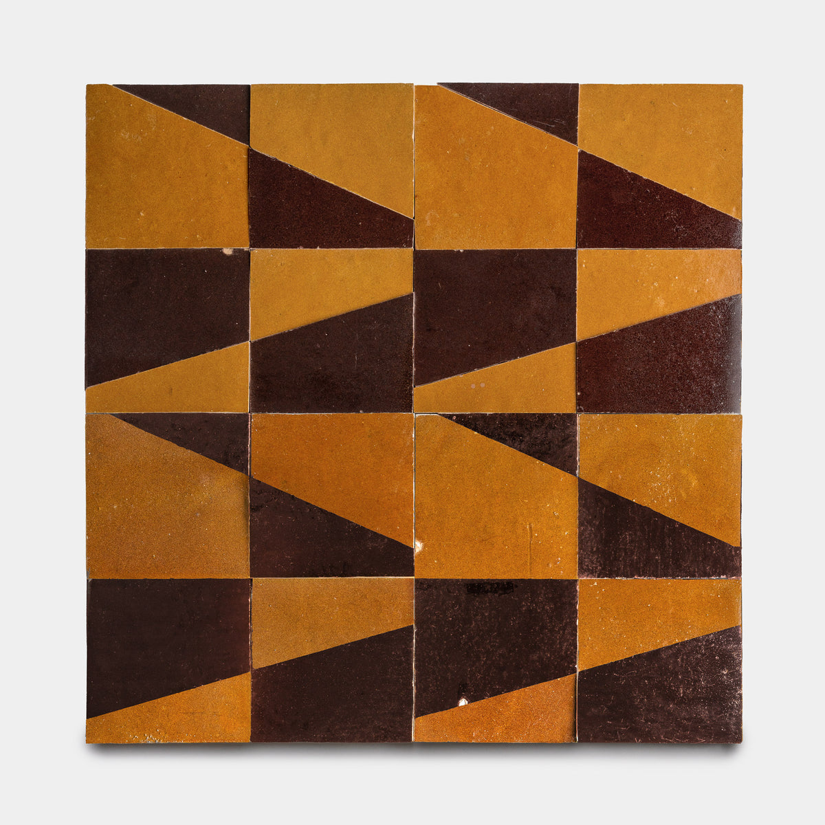 Atlas 2 by Zia Tile features four rows of four square tiles in a grid. Each tile displays an abstract, geometric motif in mustard yellow and dark brown, creating a bold, repeating pattern.