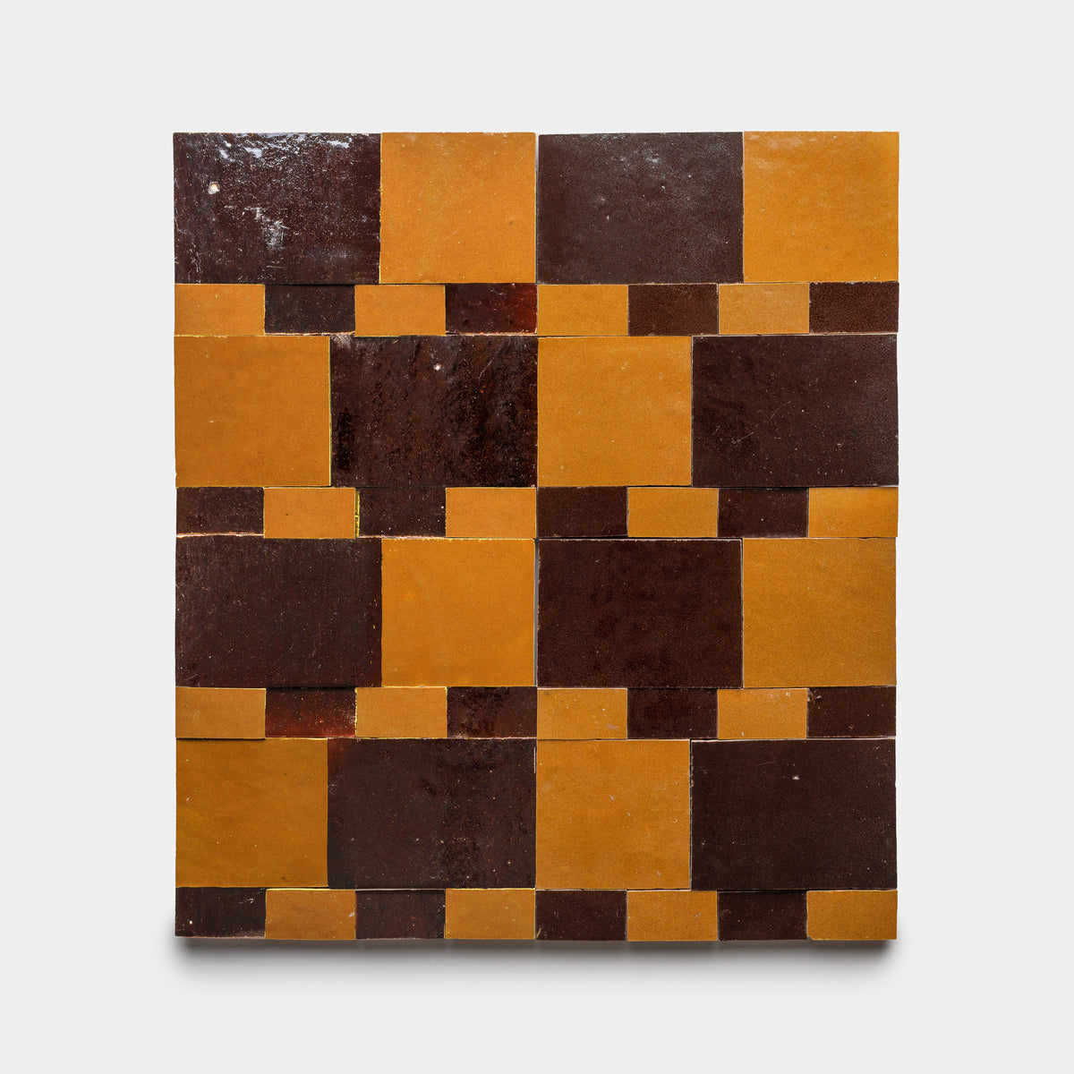 The Xylem 2 tile by Zia Tile features a geometric pattern of alternating large dark brown and mustard yellow squares, with small contrasting rectangles, arranged checkerboard-style on a plain background.