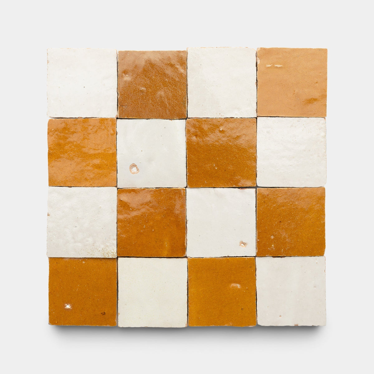 Sixteen glossy handmade tiles in a 4x4 grid, alternating between white and burnt orange, form the Amber + Casablanca Checkerboard sample by Zia Tile, showcasing their signature checkerboard style.