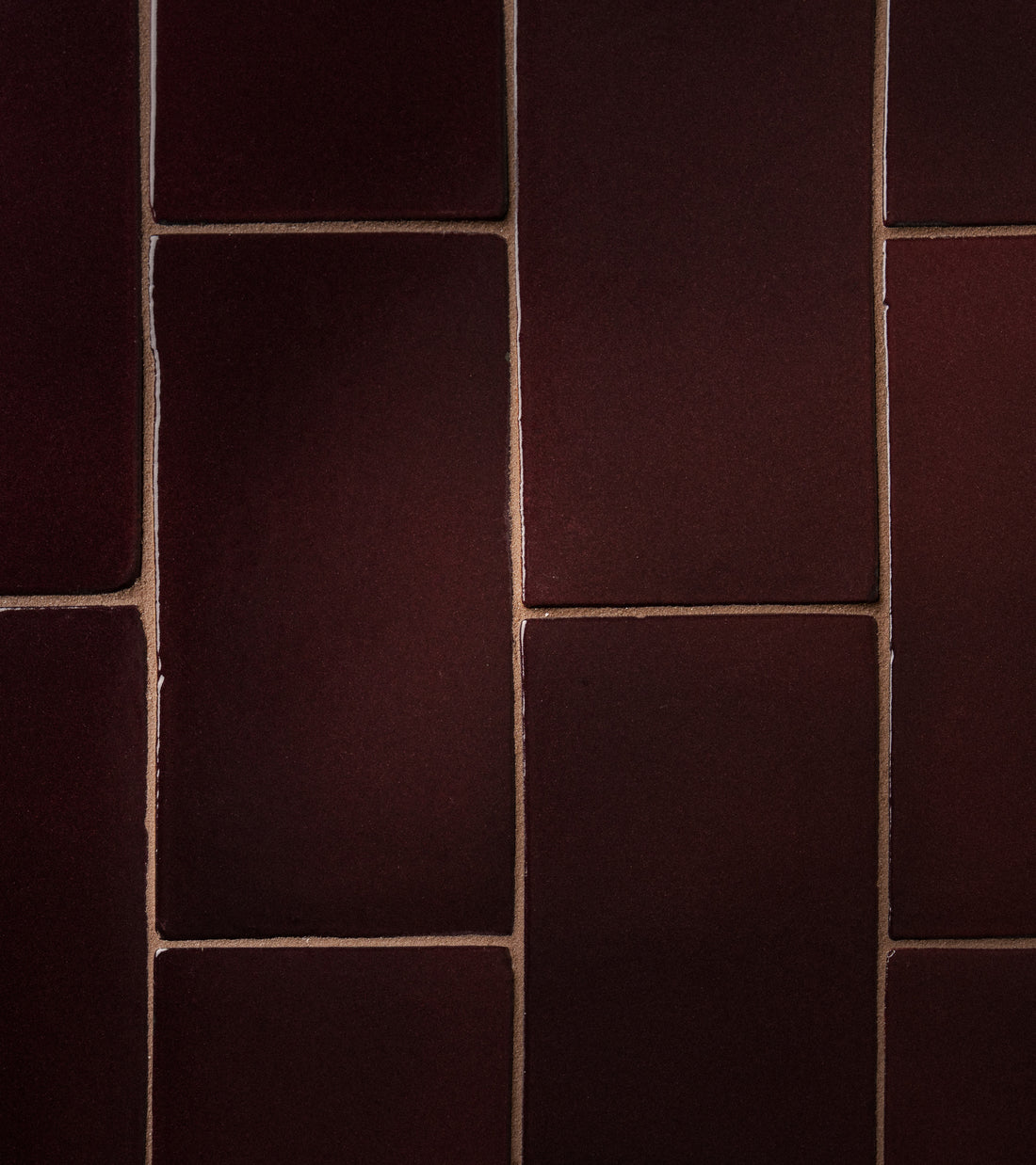 Close-up of Zia Tile's Ancho 4x8 Rectangle: reddish-brown matte tiles with visible grout lines, arranged in a staggered pattern. Subtle lighting brings out their textured surface.