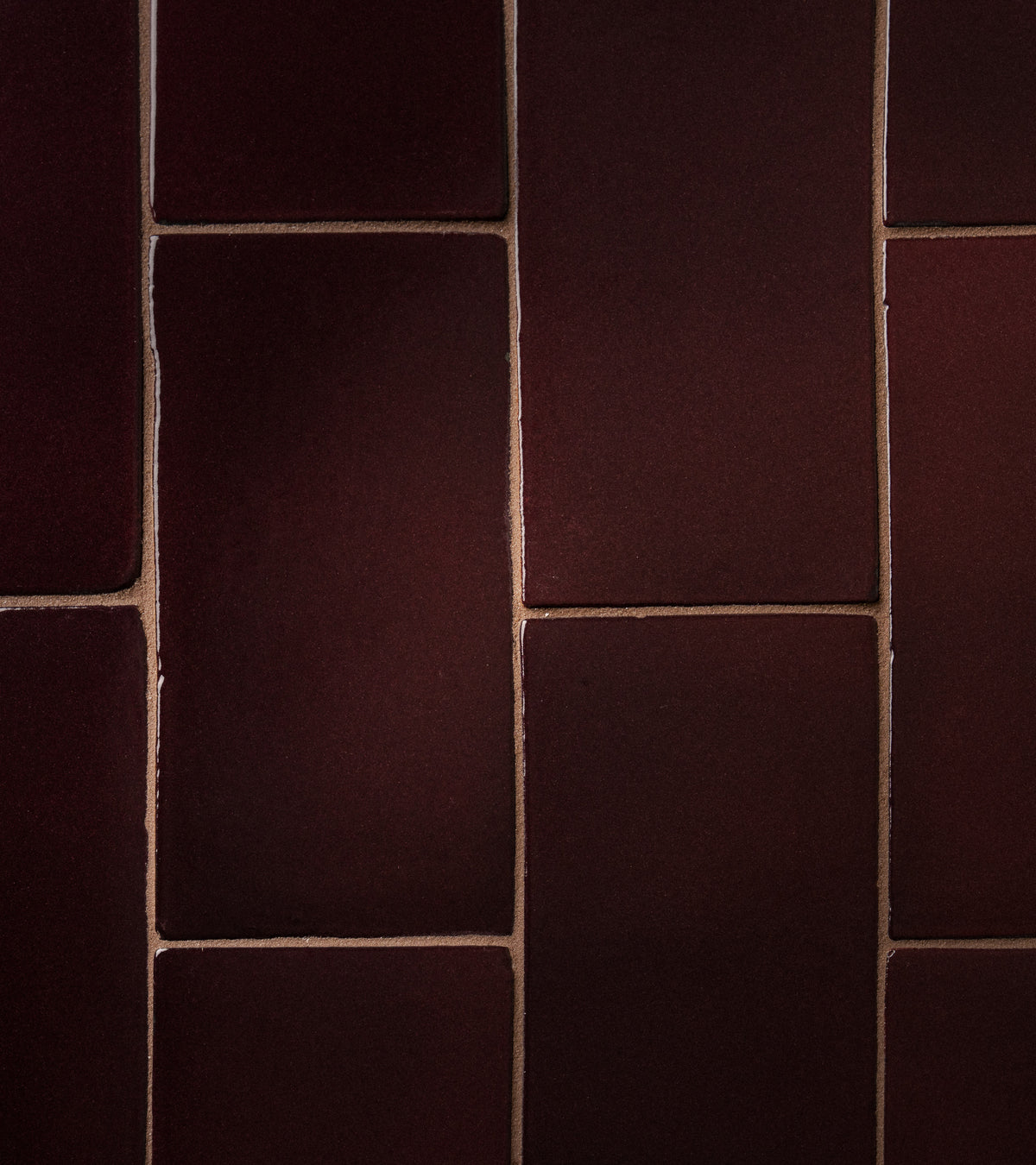 Close-up of Zia Tile's Ancho 4x8 Rectangle: reddish-brown matte tiles with visible grout lines, arranged in a staggered pattern. Subtle lighting brings out their textured surface.