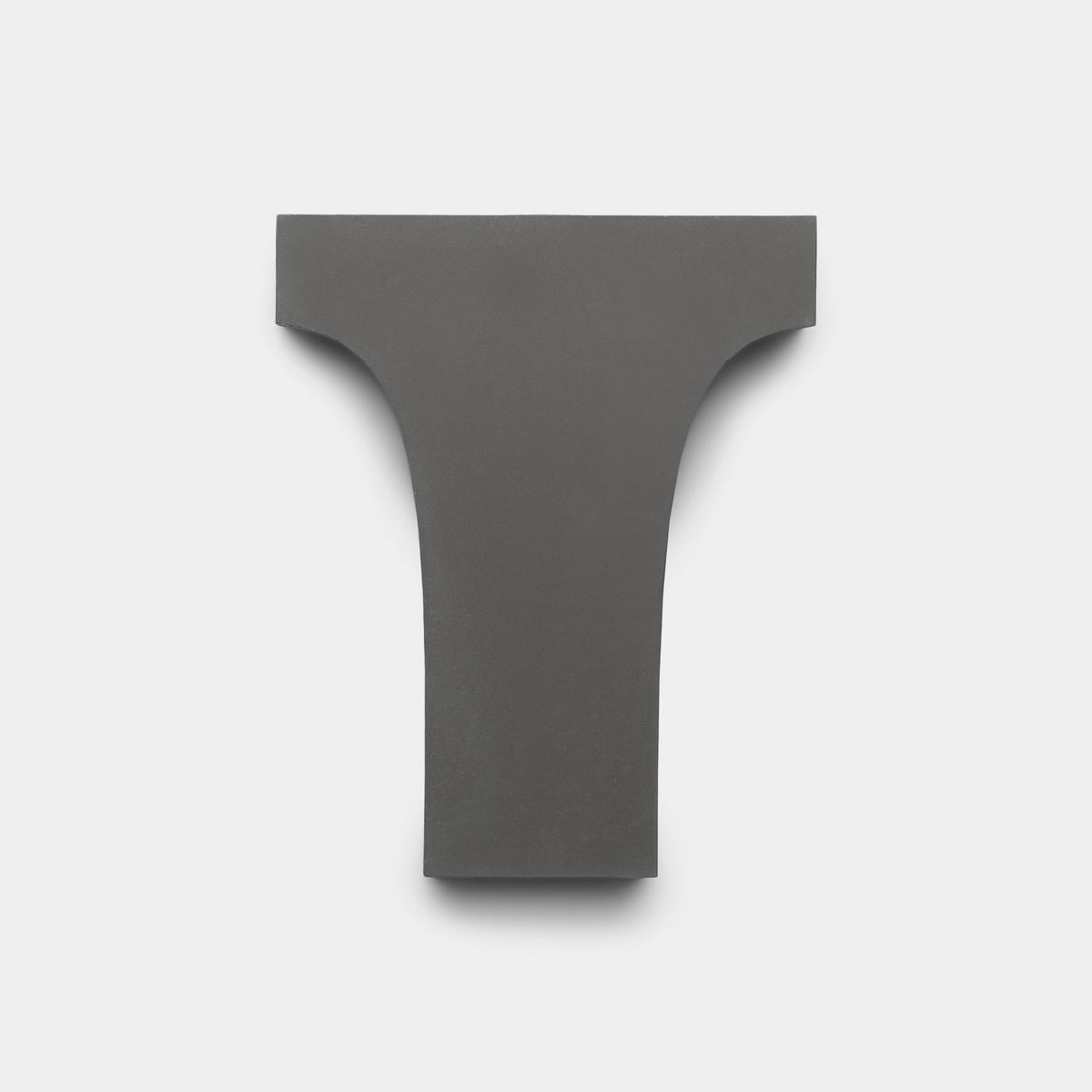 The Arco White + Black + Bone Sample by Zia Tile features a handmade, dark gray T-shaped tile with a wide, flat top and gently curved sides, shown on a plain light gray background.