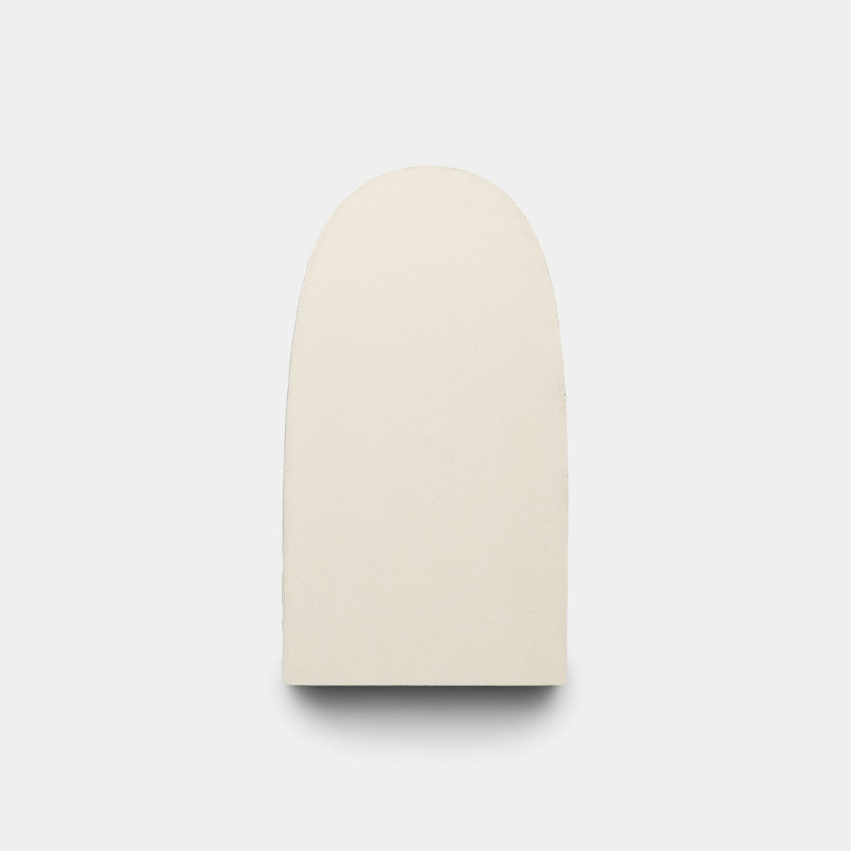 The Arco White + Black + Bone sample by Zia Tile is a handmade, off-white, rounded rectangular tile with a flat base, shown standing upright against a light gray background.