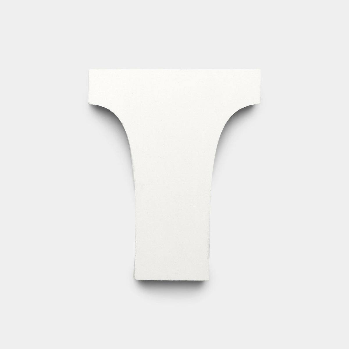 A flat, white, T-shaped cement tile from Zia Tile’s Arco White + Black + Bone collection is centered on a plain light gray background. The tile features rounded top corners and smooth cutouts, highlighting its handmade design.