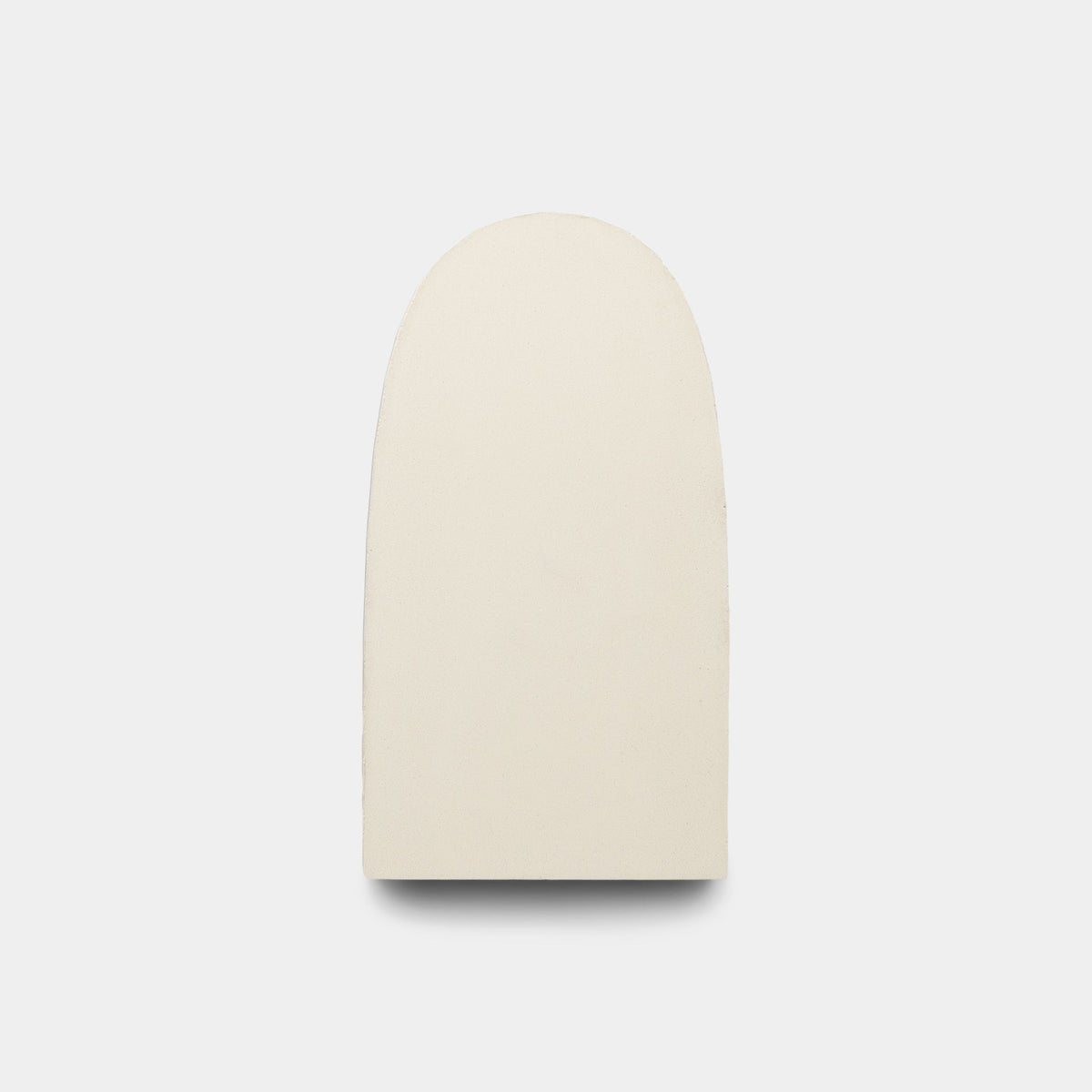 A plain, smooth, off-white “Arco White + Bone” sample by Zia Tile with a rounded top and flat bottom, centered on a light gray background reminiscent of handmade Zia Tile surfaces.