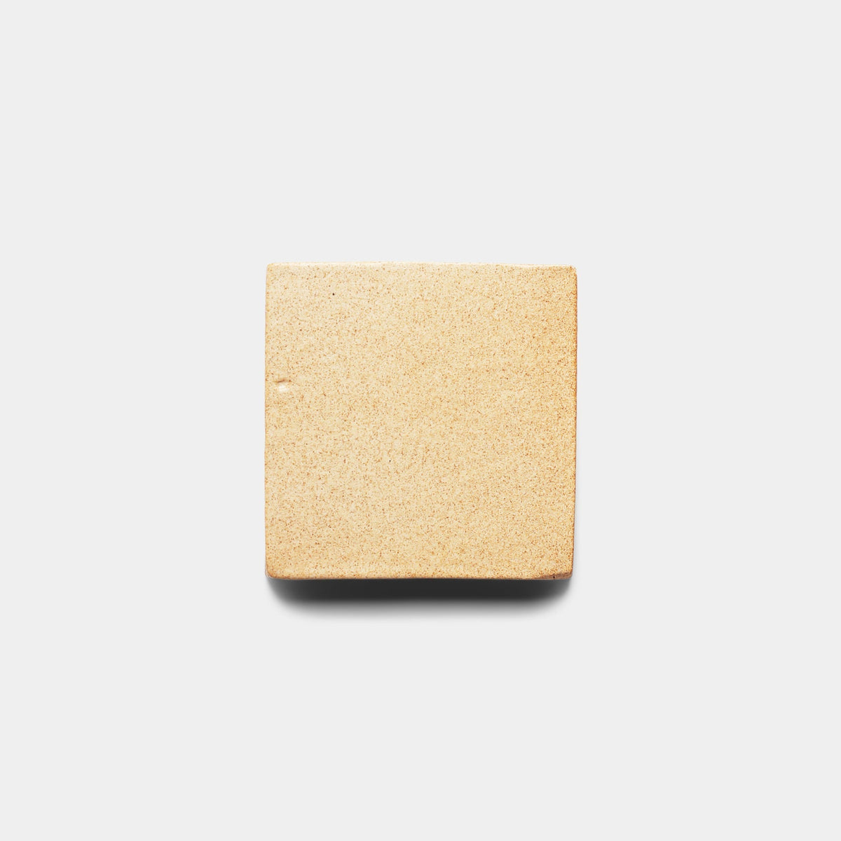 A beige Arroyo 4x4 Square tile sample from Zia Tile sits on a plain white background, casting a subtle shadow—its smooth finish evokes handcrafted artisan quality.