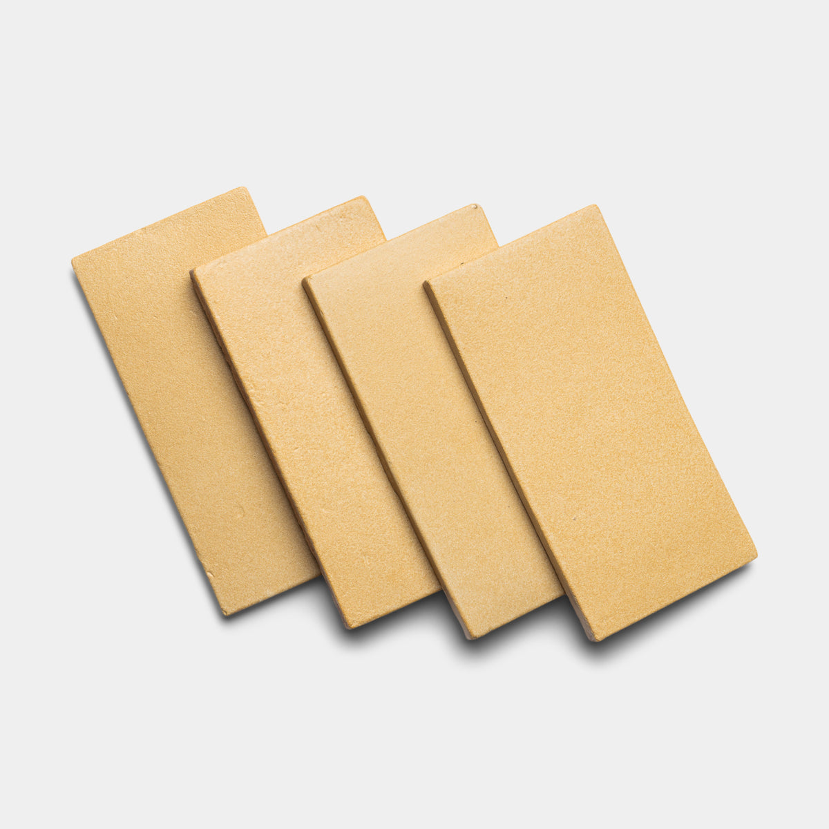 Four Arroyo 4x8 Rectangle tiles by Zia Tile, tan in color, are arranged in a slightly overlapping, fanned-out pattern on a white background.