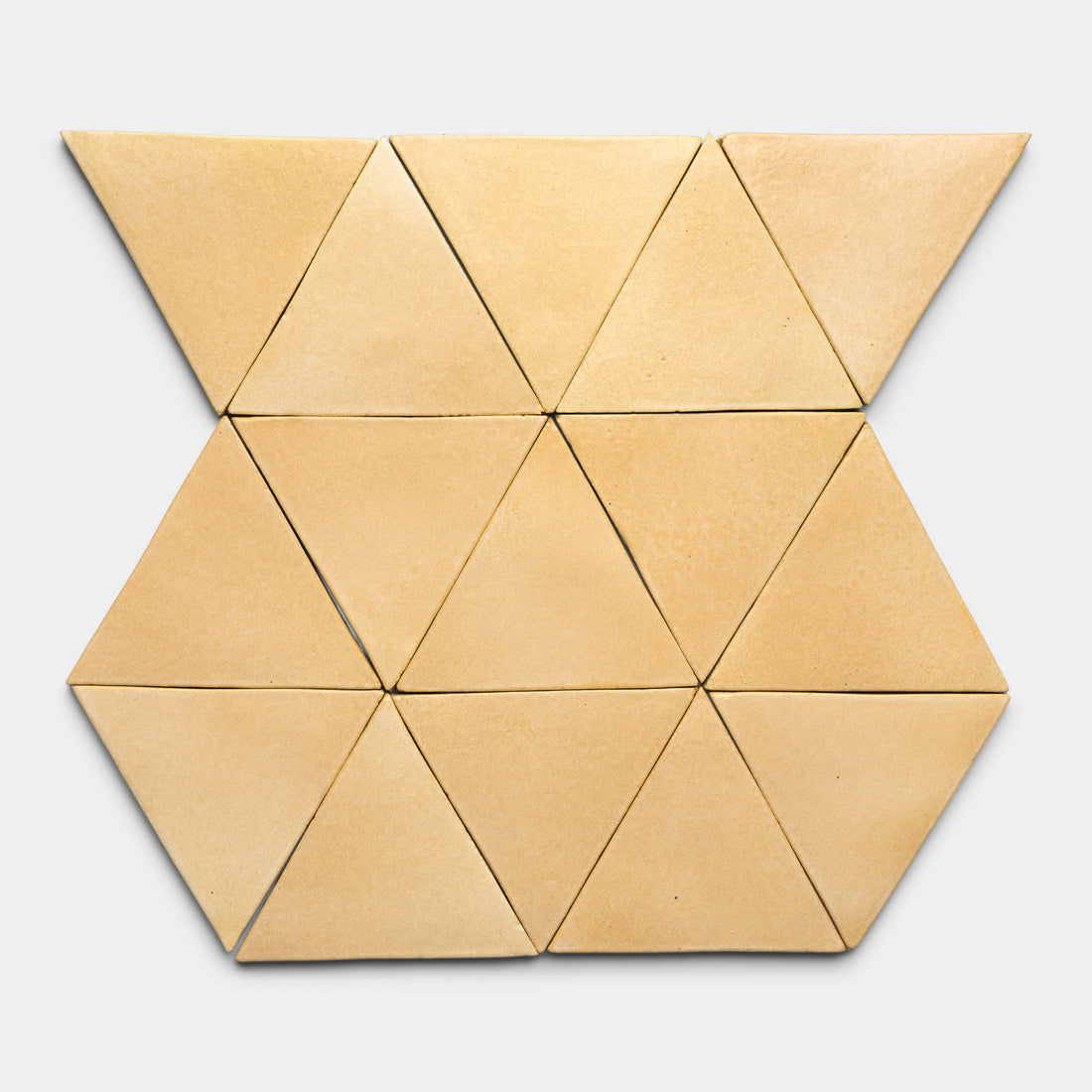 Twelve tan Arroyo Triangle tiles by Zia Tile are arranged on a light gray background, forming a symmetrical, geometric pattern with striking tessellation.