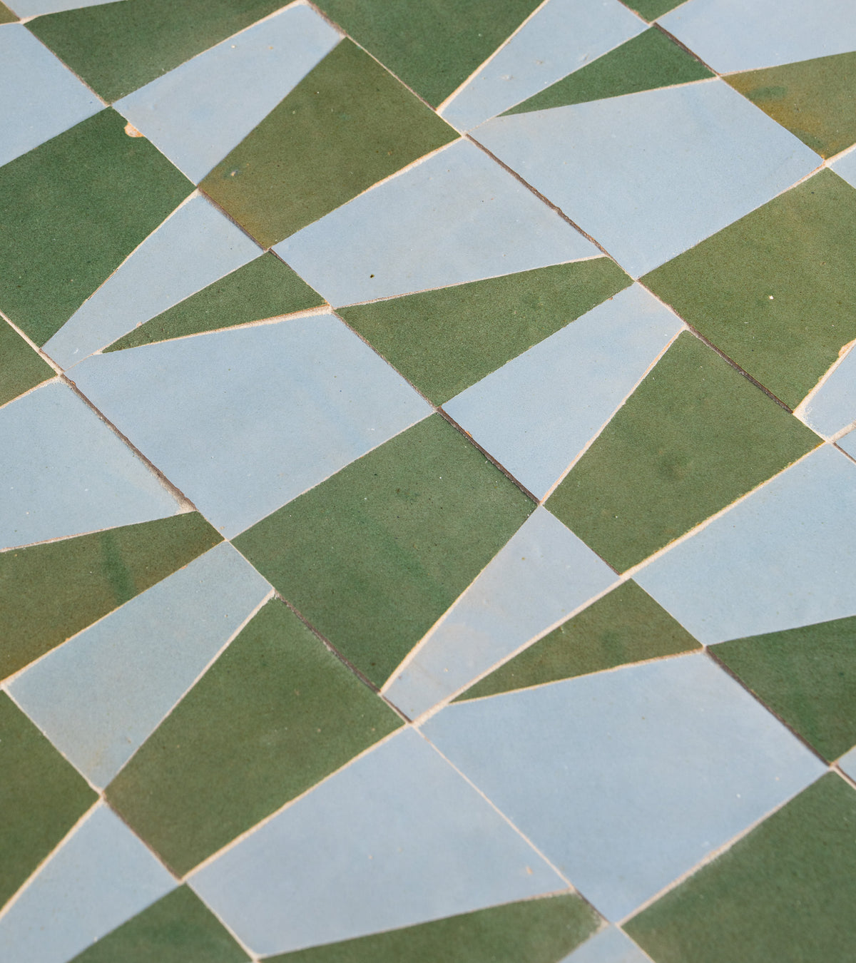 A close-up of Zia Tile’s Atlas 3 shows patterned tiles in green and light blue forming an abstract geometric mosaic, with visible grout lines between the tiles.